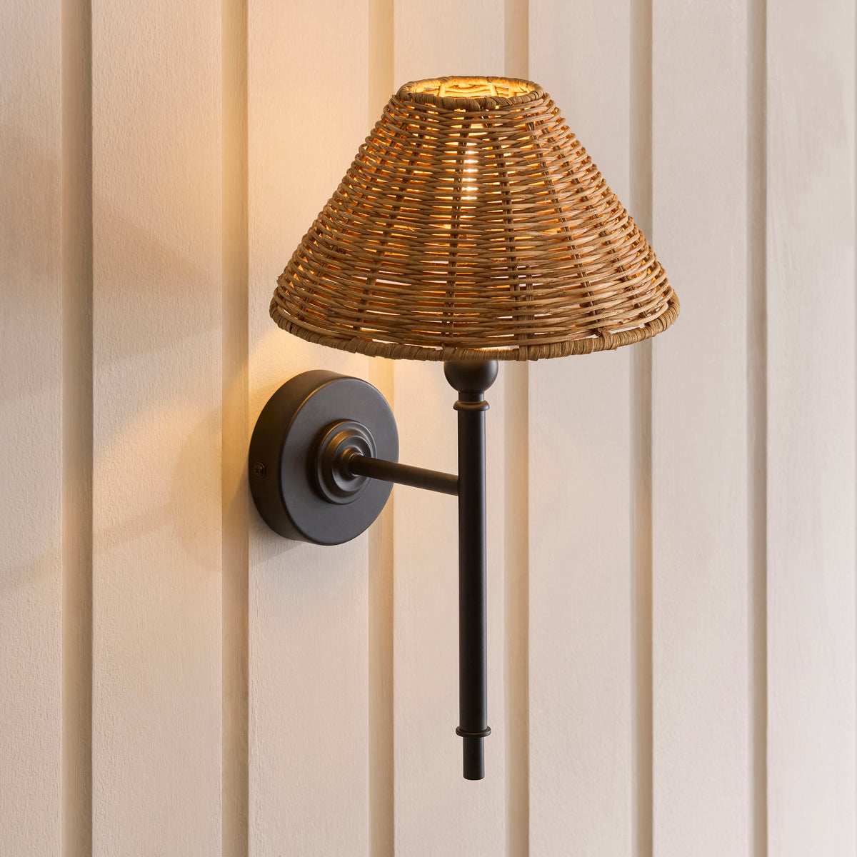 Jericho matt black wall light glowing against panelling, rattan shade casting warm light