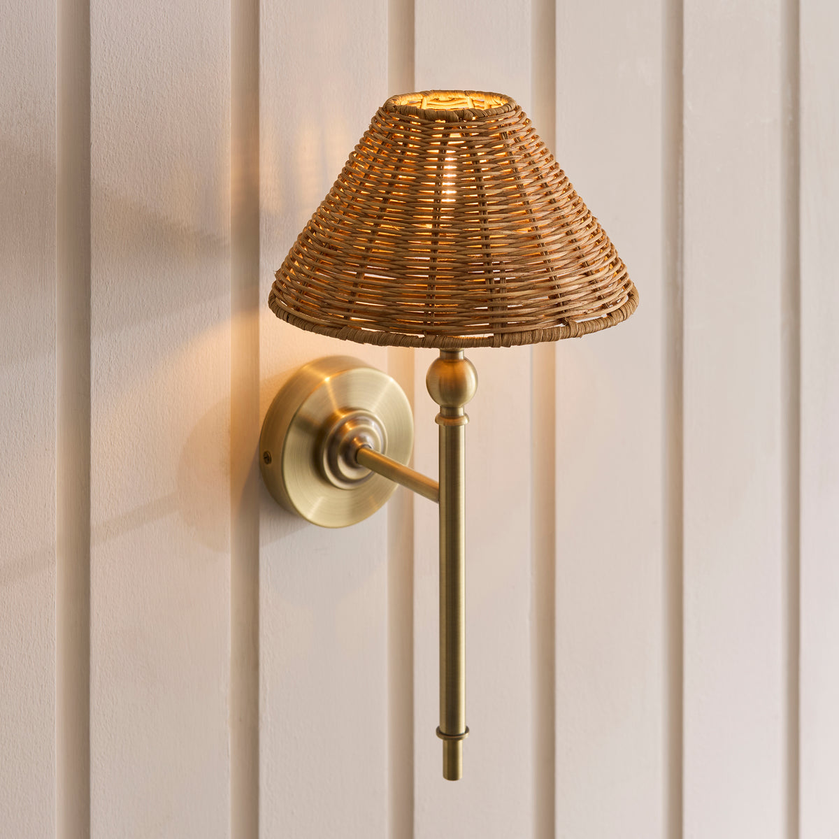 Close-up of the Jericho wall light's lit rattan shade above its brass ball-detailed stem