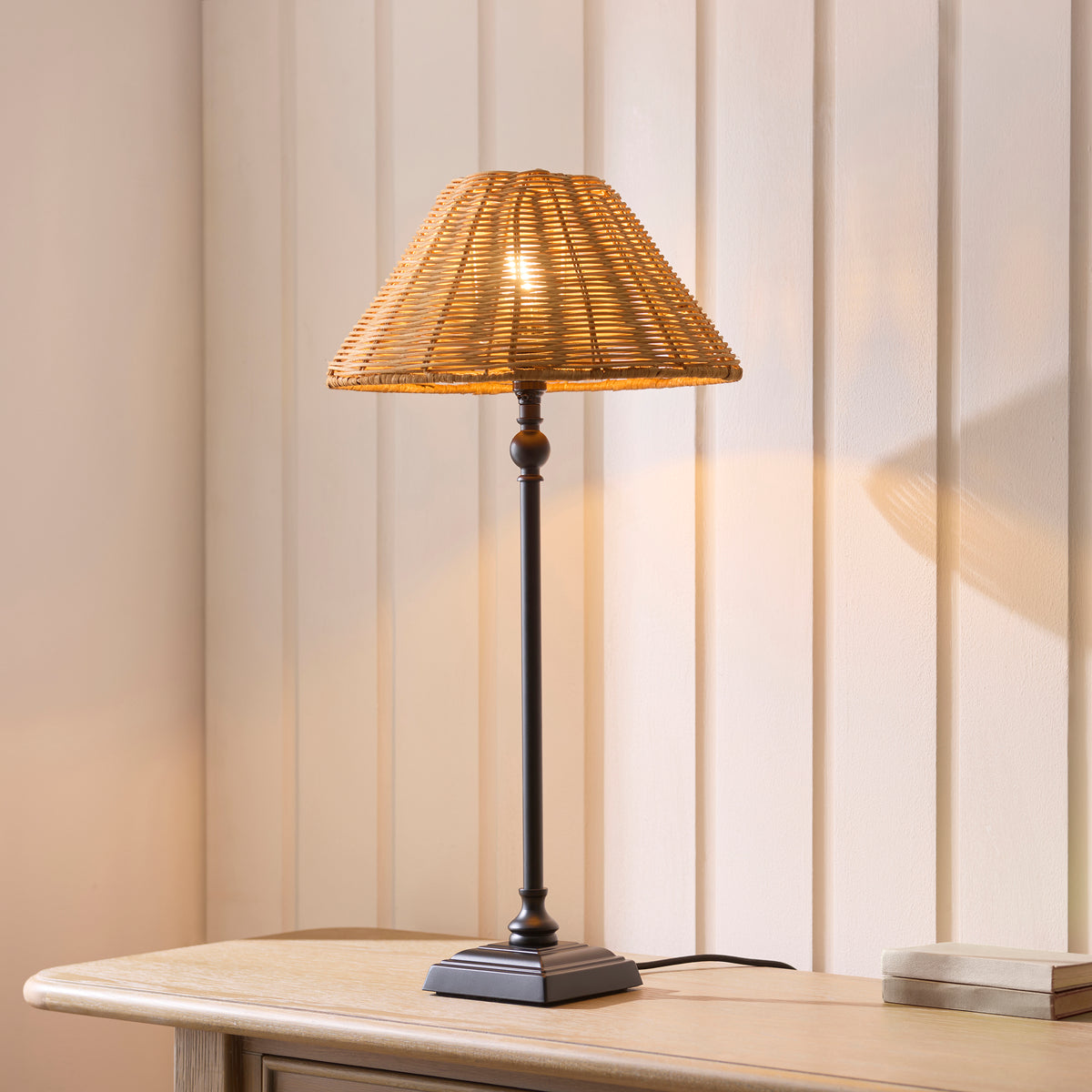Jericho black rattan table lamp lit on a painted wooden chest of drawers