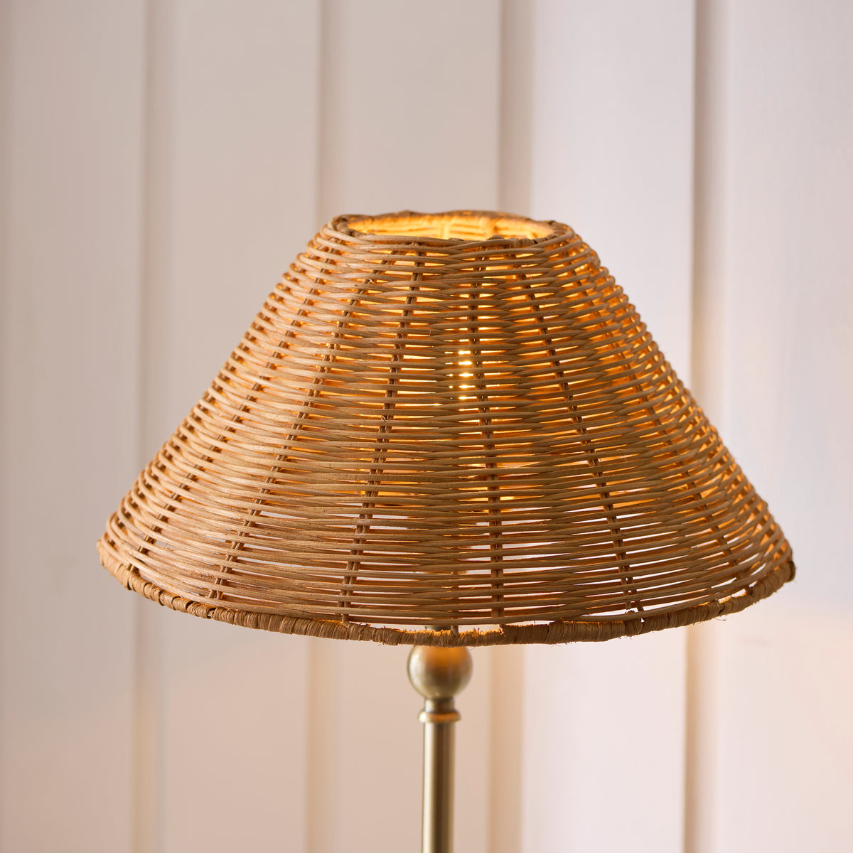 Close-up of the Jericho lamp's natural rattan coolie shade lit above a brass stem