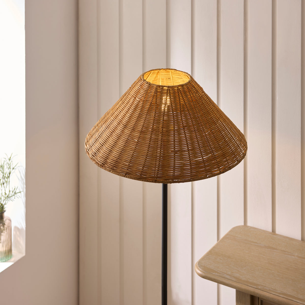 Wide woven rattan shade of the Jericho floor lamp lit against cream panelling