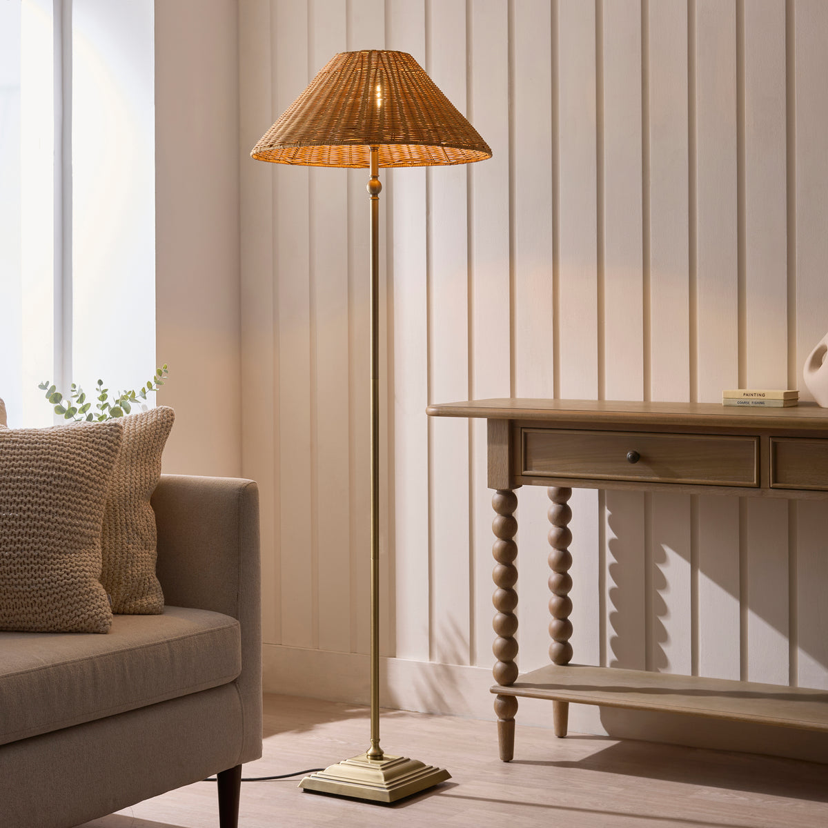 Jericho brass floor lamp lighting a living room beside a cream sofa and oak console table