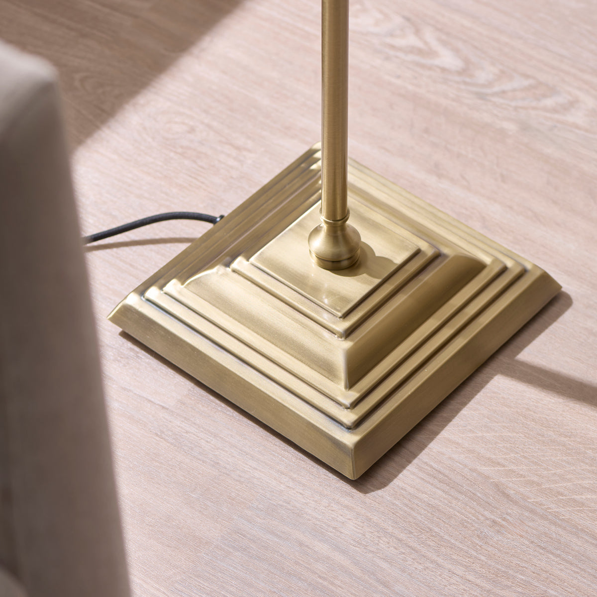 Stepped square antique brass base of the Jericho floor lamp on pale wood flooring
