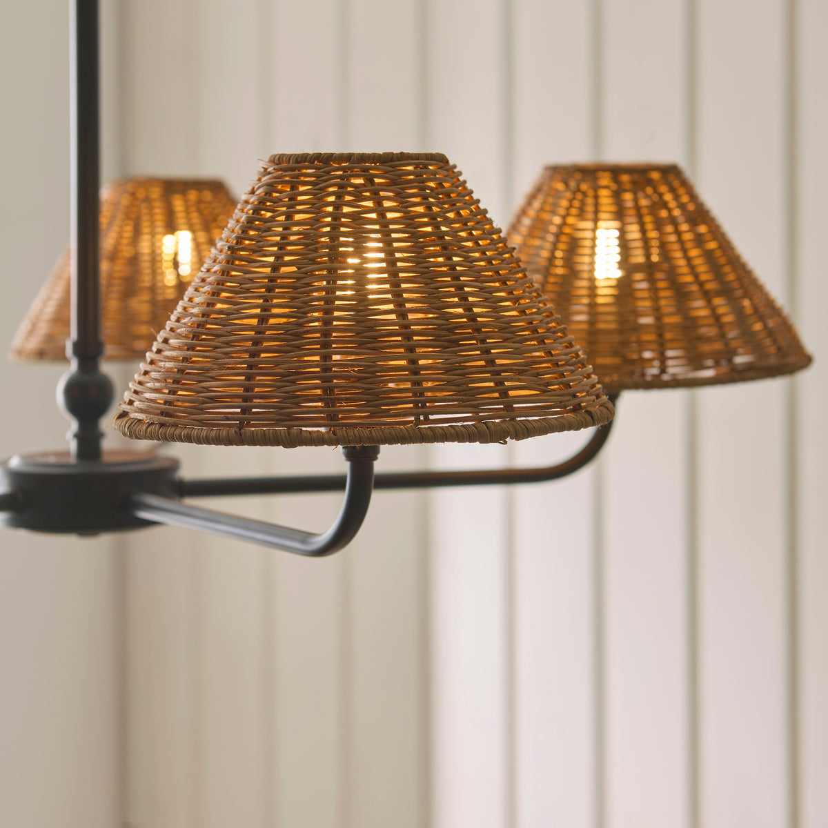 Close-up of three glowing brown rattan shades on the Jericho black pendant