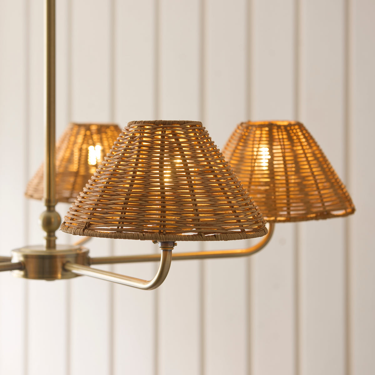 Three lit brown rattan shades on the brass arms of the Jericho chandelier