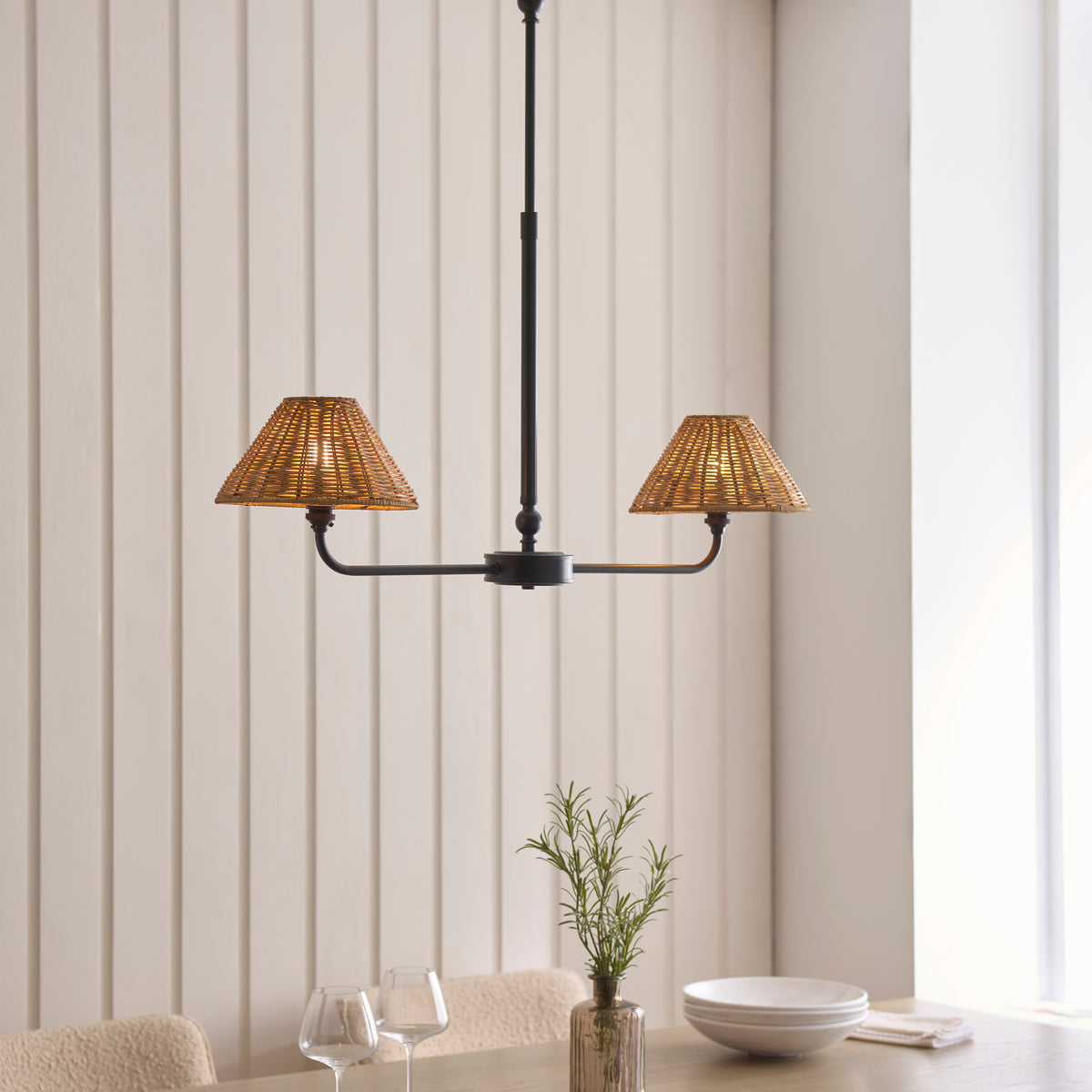 Jericho black linear rattan pendant lit above a dining table set with wine glasses and a bowl