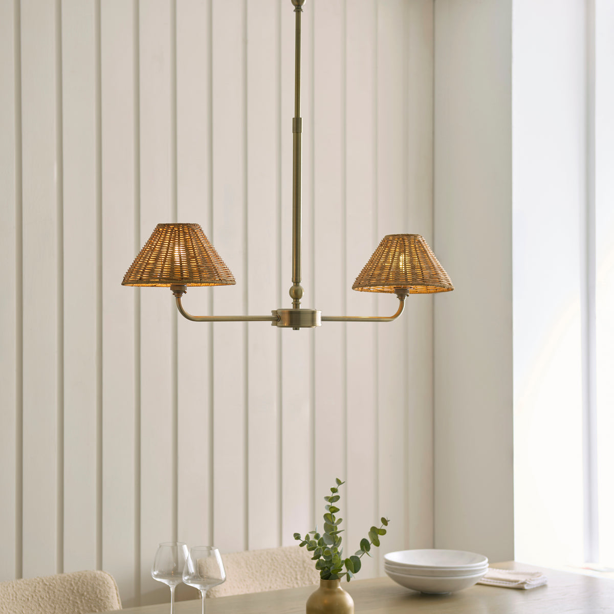 Jericho brass linear rattan pendant lit over a dining table with glasses and a bowl