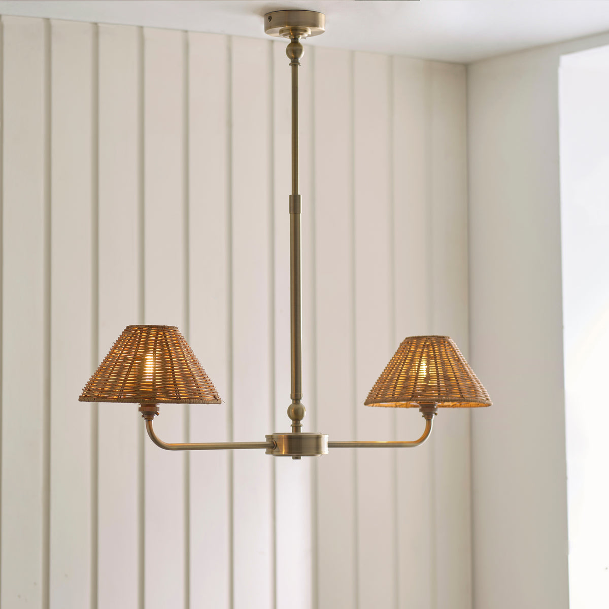 Two-light Jericho brass linear pendant with rattan shades against cream panelling