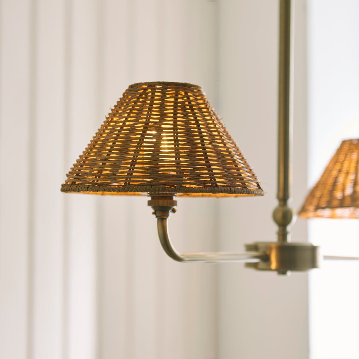 Close-up of a lit brown rattan shade on the brass arm of the Jericho linear pendant