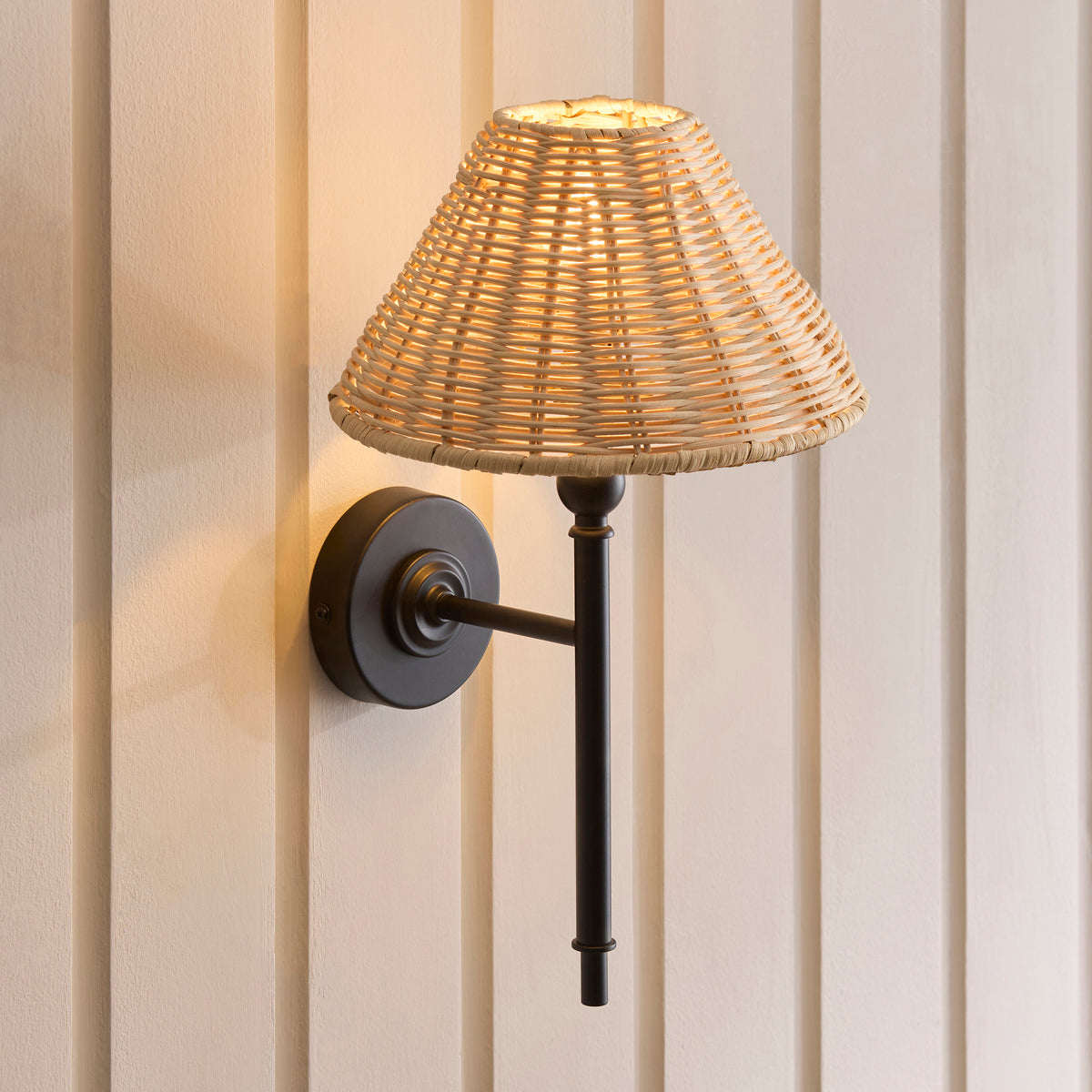 Angled view of the Jericho matt black wall light casting warm light on panelled walls