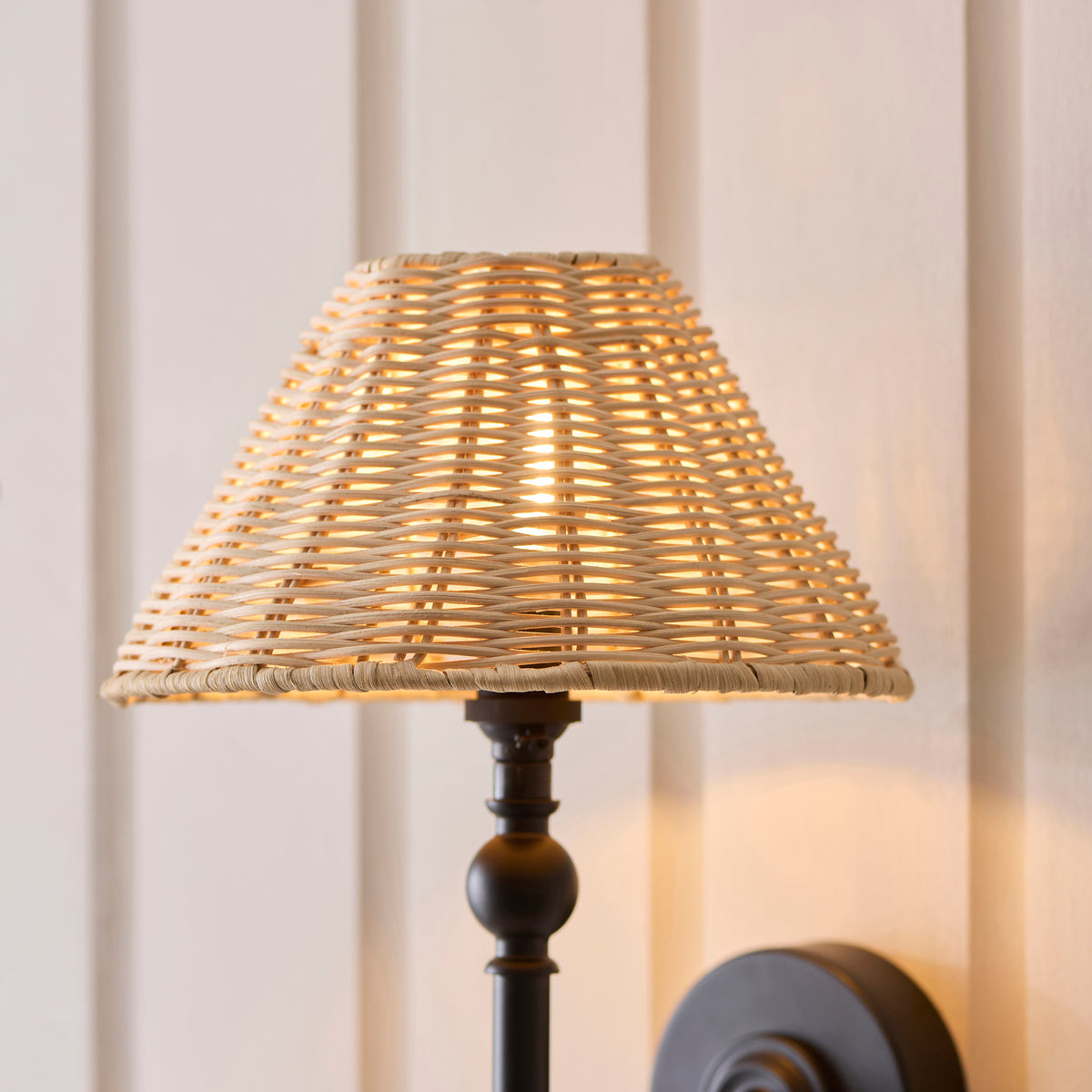 Close-up of the Jericho wall light's natural rattan shade glowing above its black stem