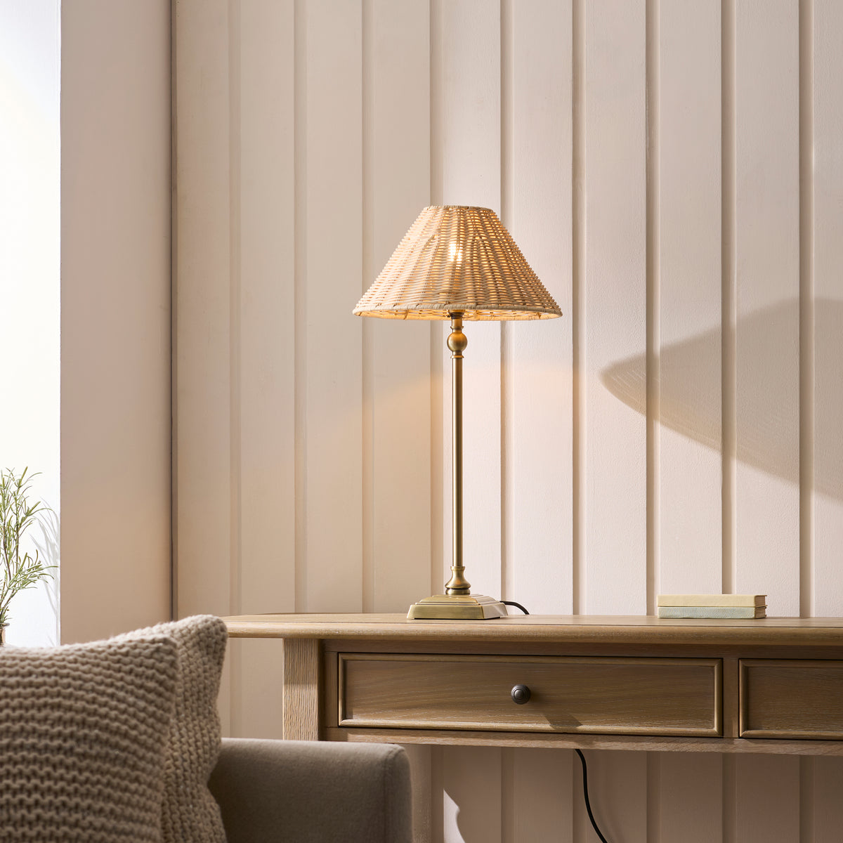 Jericho antique brass table lamp lit on a wooden console table beside a knitted cushion and panelled wall