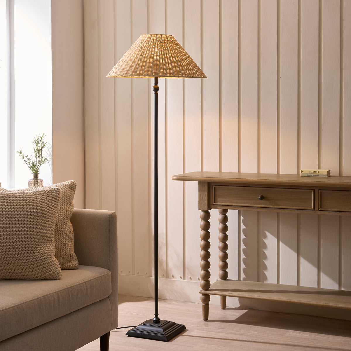 Jericho black floor lamp lit in a living room beside a cream sofa and spindle console table