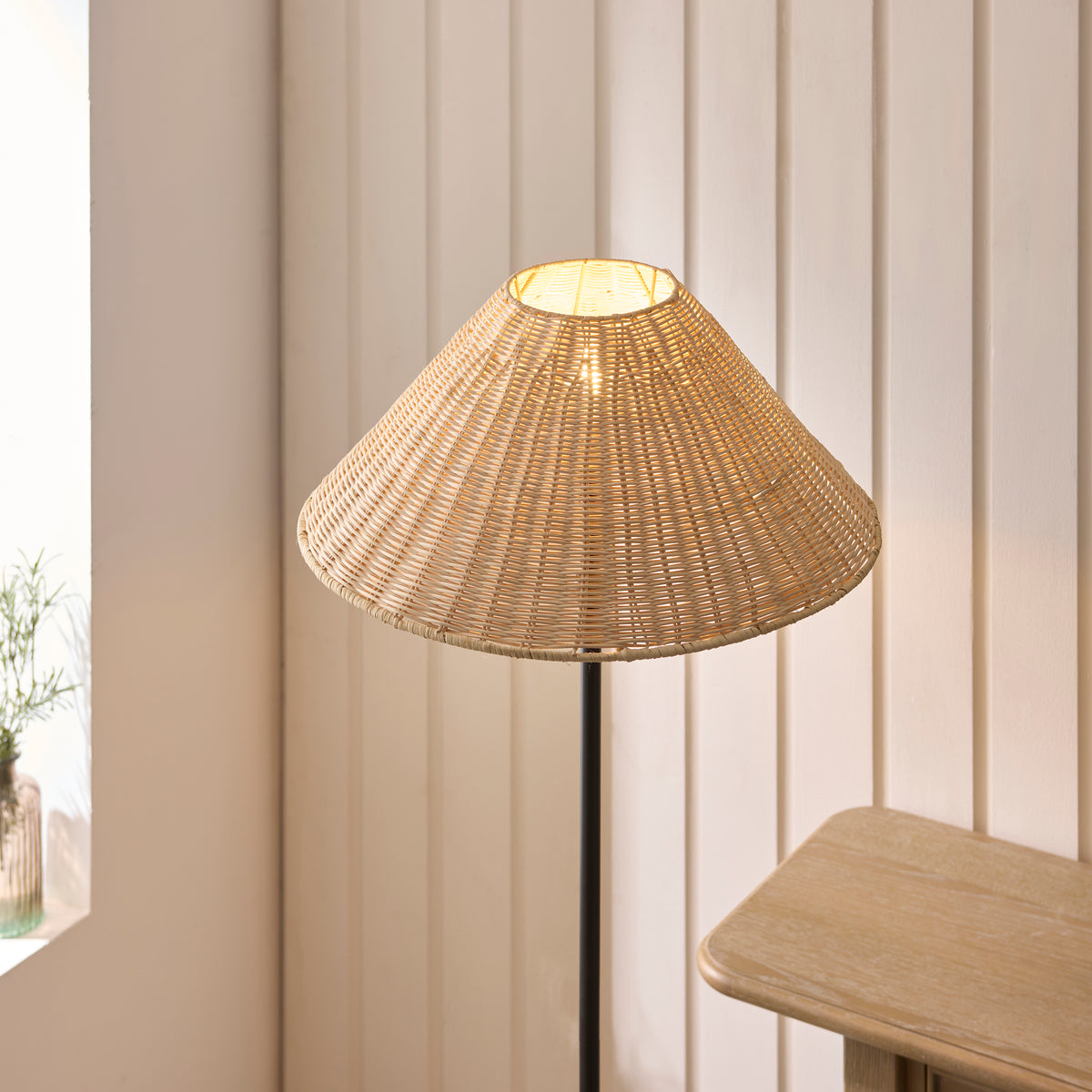 Illuminated natural rattan coolie shade of the Jericho black floor lamp against panelled walls