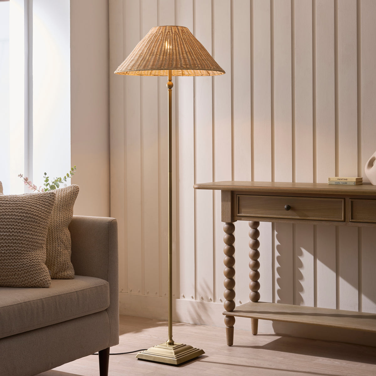 Jericho brass floor lamp lit beside a cream sofa and bobbin-legged console table by a window