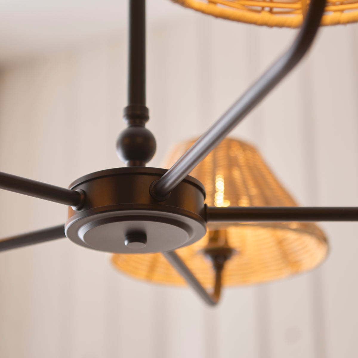 Black centre hub and arms of the Jericho pendant seen from below with lit rattan shade behind