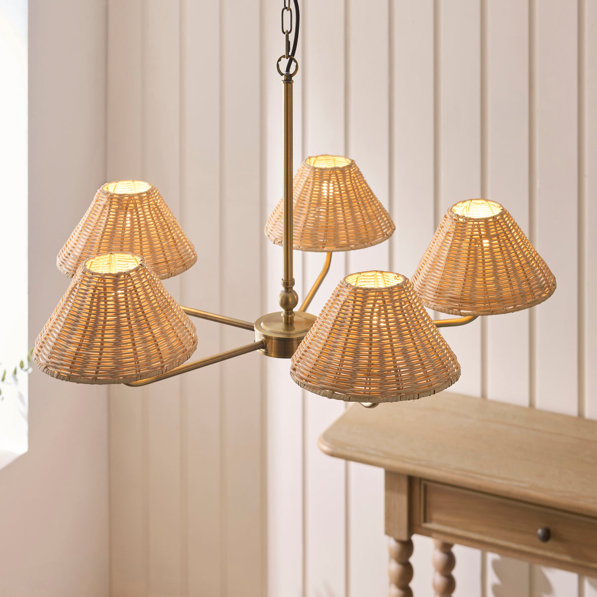 Lit Jericho antique brass chandelier with five woven rattan shades by a bright window