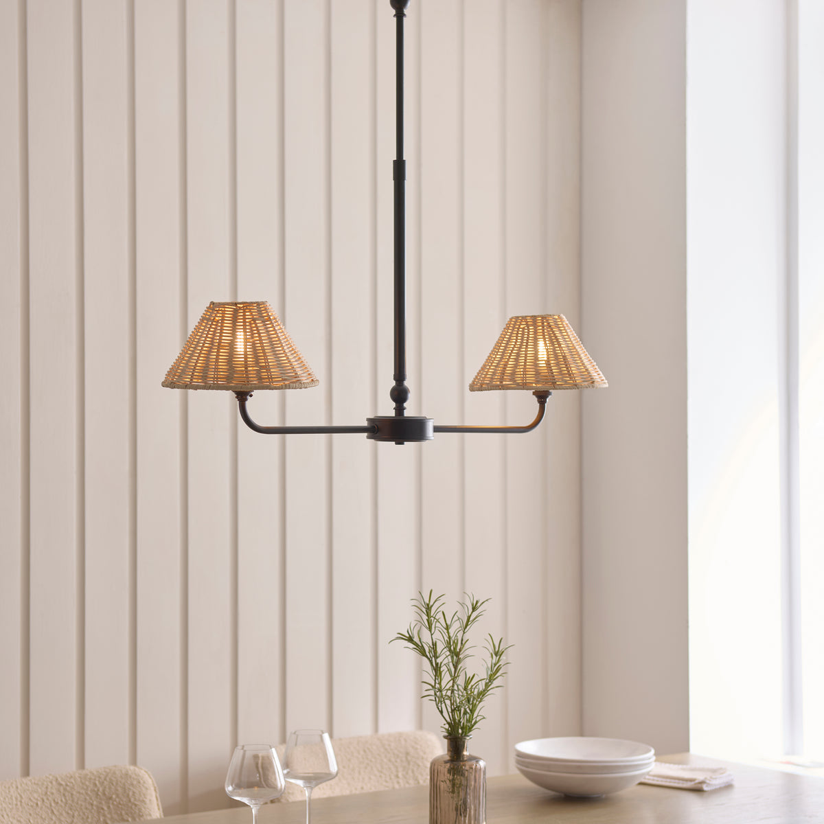 Jericho black linear pendant lit above a dining table set with glasses and a bowl
