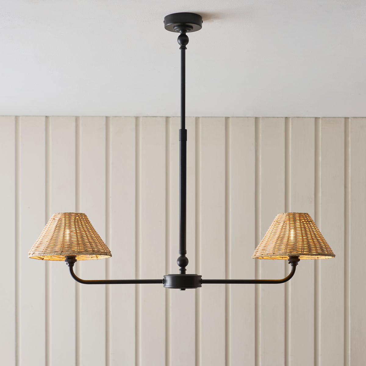 Lit Jericho black linear pendant with two woven rattan shades against pale panelling