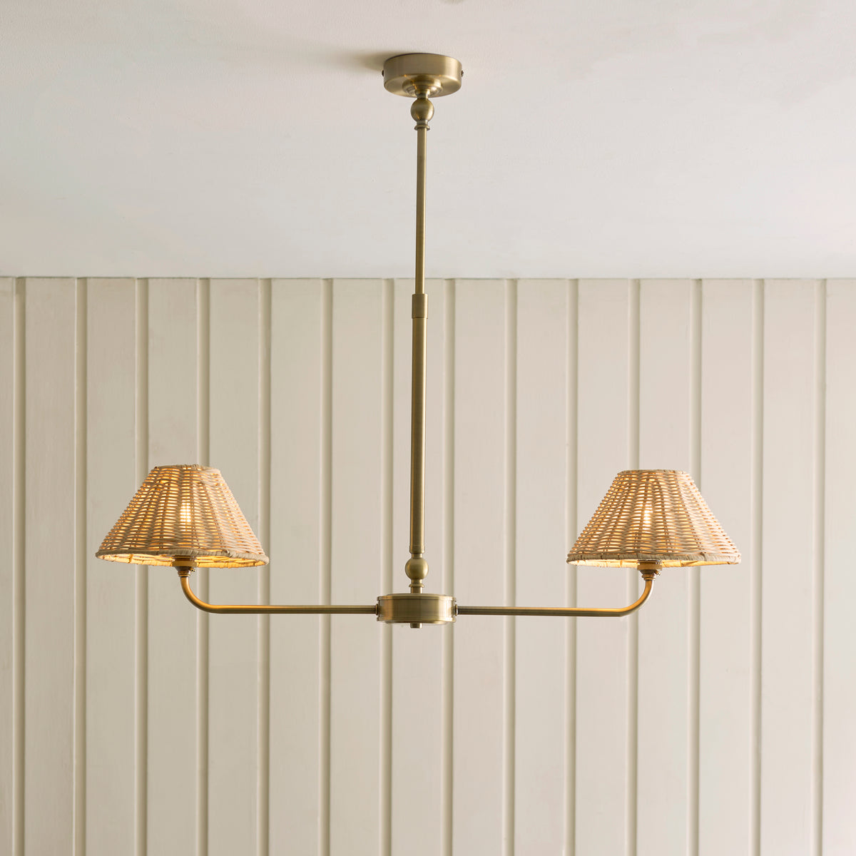 Lit Jericho brass linear pendant with two woven rattan shades against cream panelling
