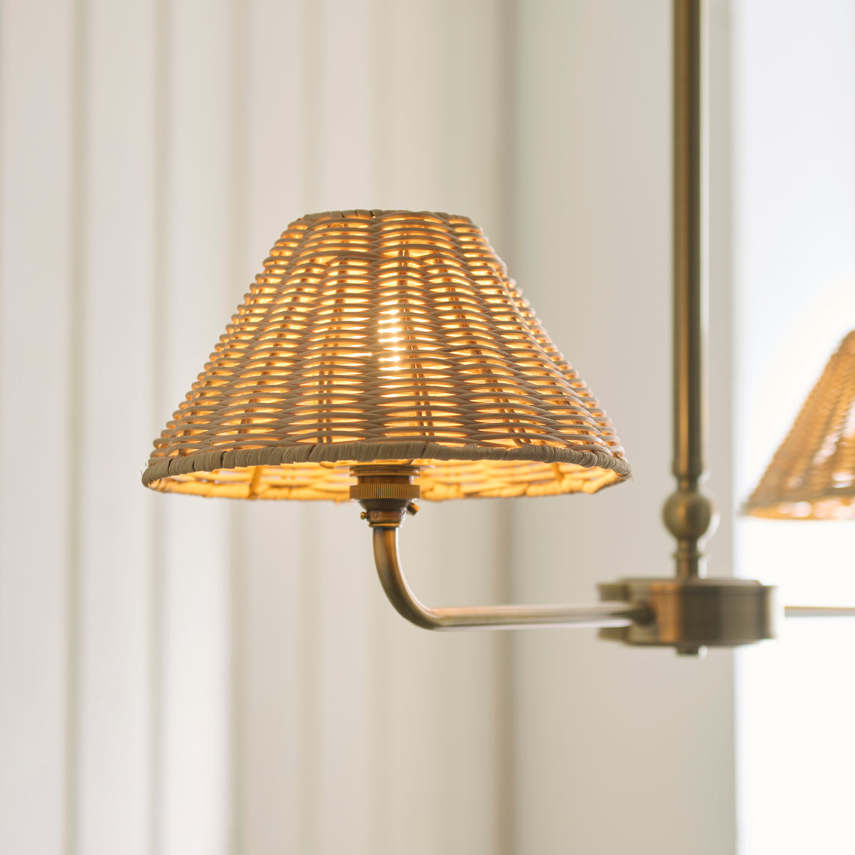 Close-up of a glowing rattan coolie shade on the Jericho antique brass linear pendant