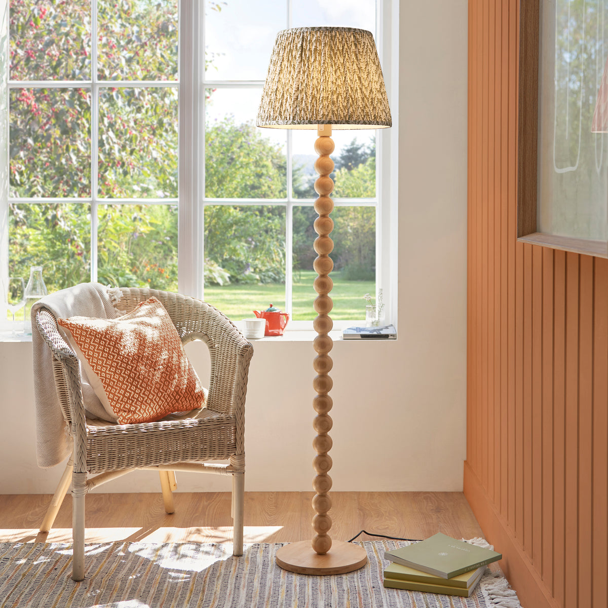 Cane & Leaf floor lamp lit by a garden window beside a wicker armchair and striped rug