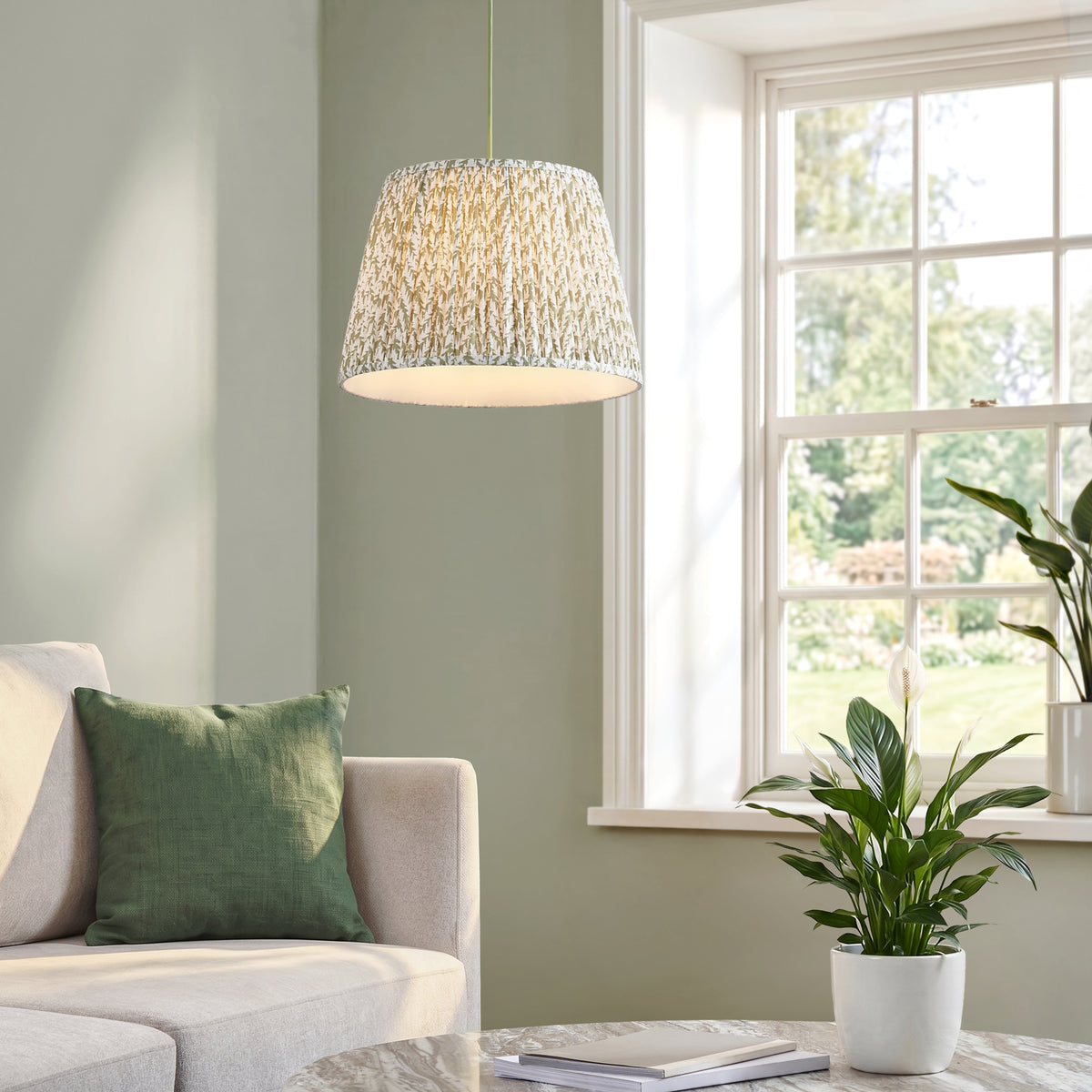 Eltham & Leaf pendant hanging in a sage green living room above a cream sofa, beside a window and houseplants
