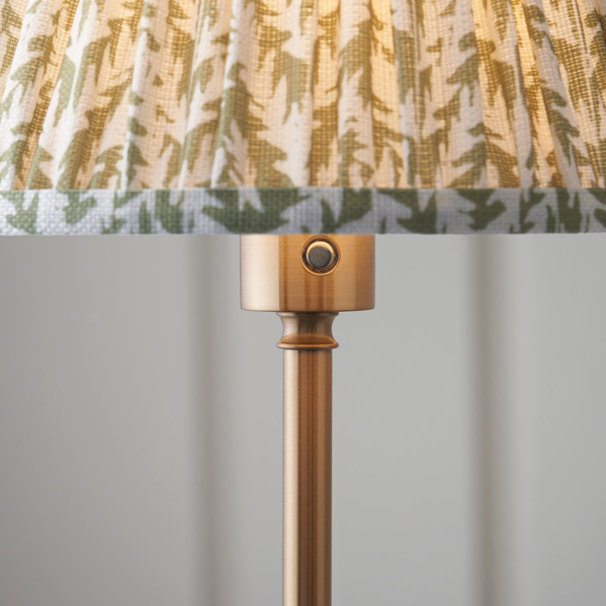 Close-up of the Burley lamp's brass shade collar, push switch and leaf-print pleated shade