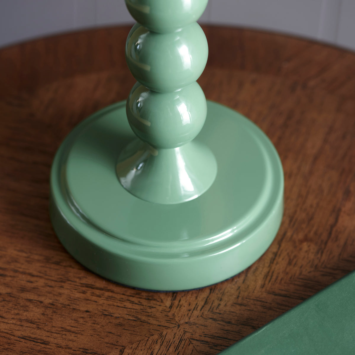 Round green base of the Higgledy table lamp resting on a polished wooden table