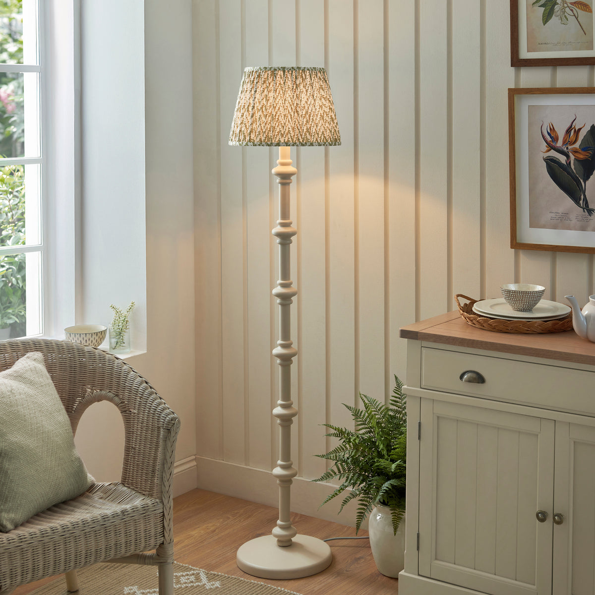 Carnaby white floor lamp lit in a panelled room beside a cream sideboard and wicker chair
