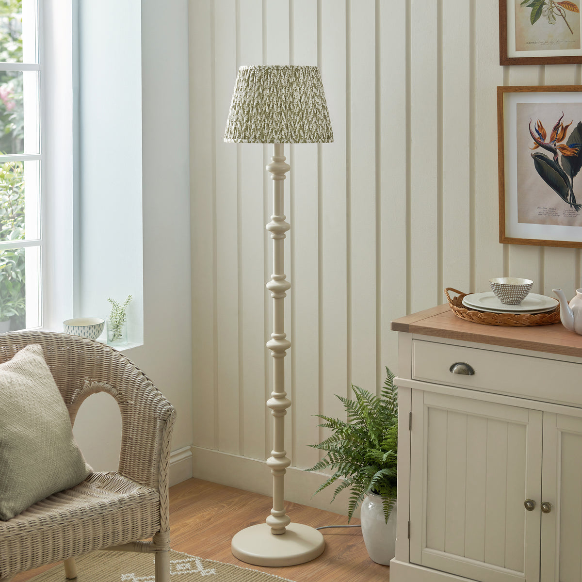 Carnaby almond white floor lamp unlit next to a sideboard, botanical prints and fern