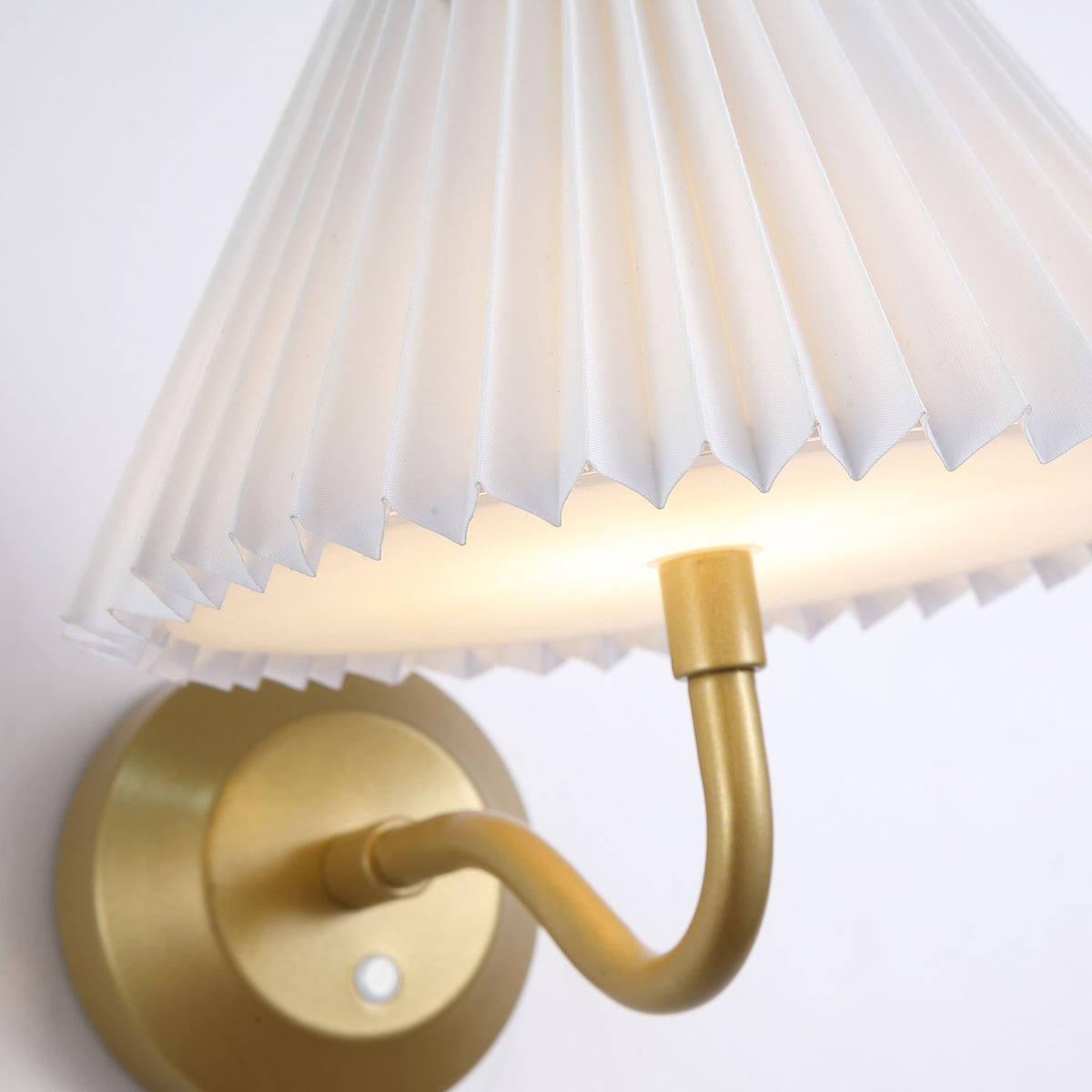 Close-up of the Danish light's brushed gold curved arm meeting its crisp pleated white shade