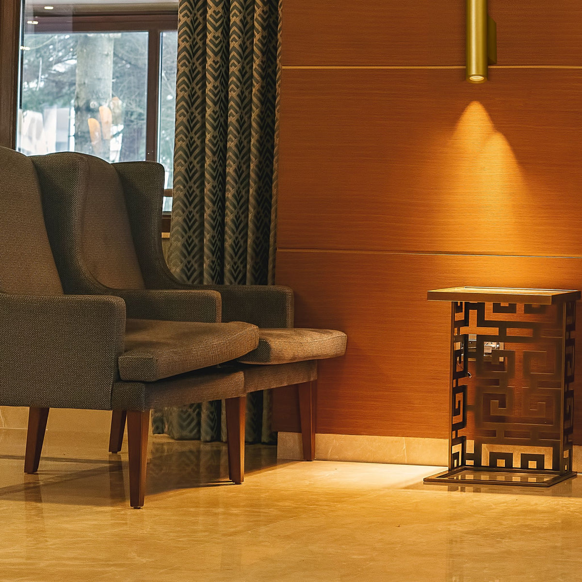 Beacon gold wall light washing a warm beam down a hotel lounge wall beside armchairs and a fretwork side table