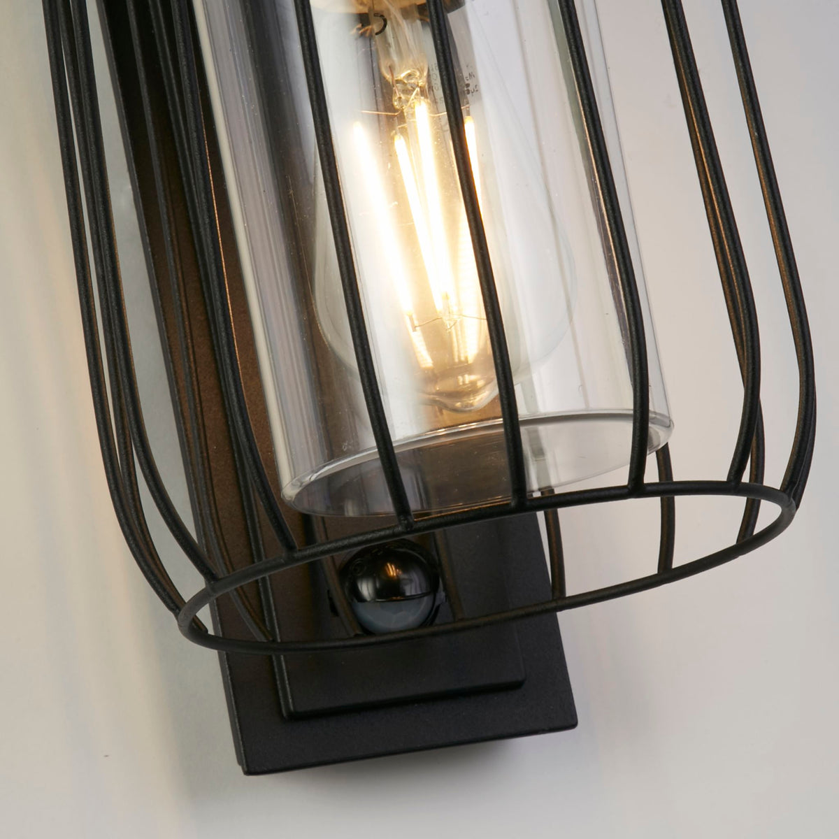Close-up of the Reed wall light's black wire cage glass cylinder and PIR sensor