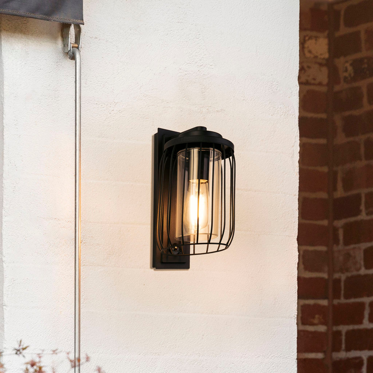 Reed black PIR wall lantern lit on a rendered exterior wall beside red brickwork
