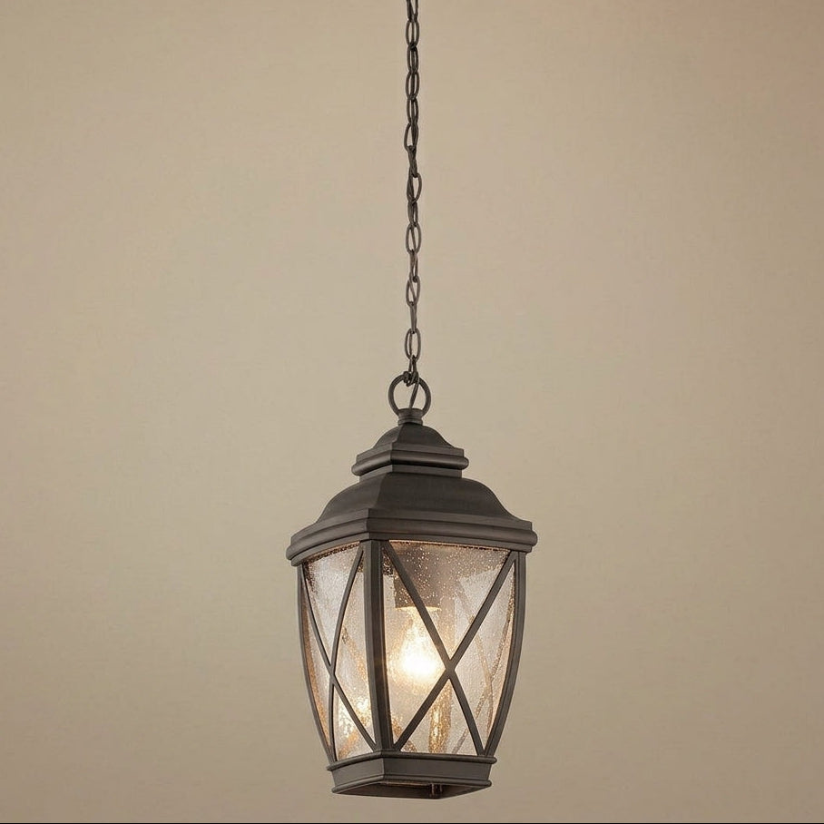 A hanging lantern-style pendant light with a dark metal frame and textured glass panels, suspended by a chain against a plain beige wall.