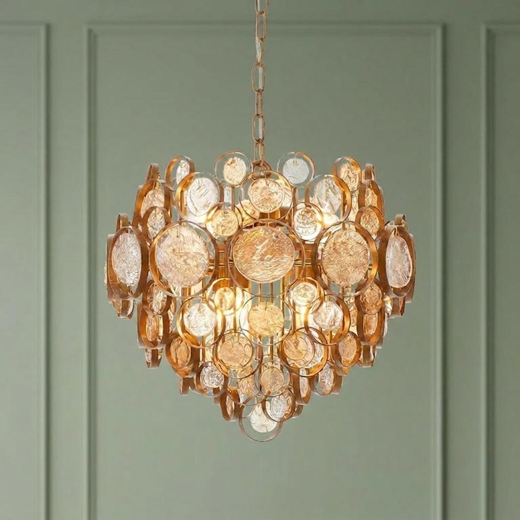Modern antique gold pendant light with amber glass discs hanging against a pale green paneled wall.