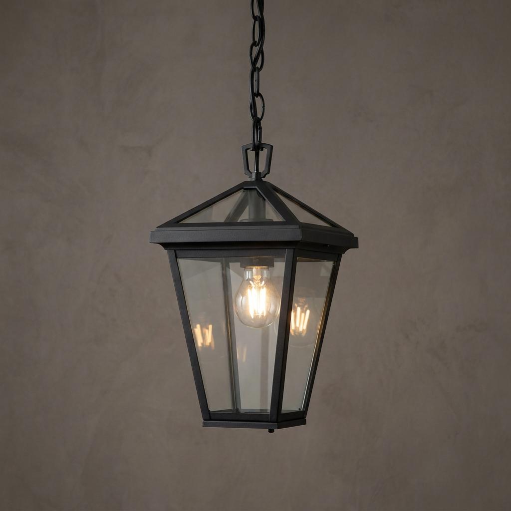 Black outdoor hanging lantern with clear glass panels and a glowing bulb against a textured wall.