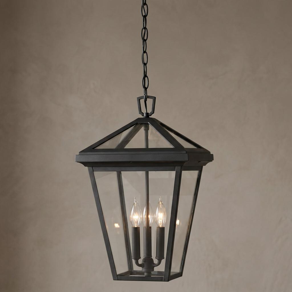 Black three-light chain lantern with clear glass panels and lit candelabra bulbs against a textured neutral wall.