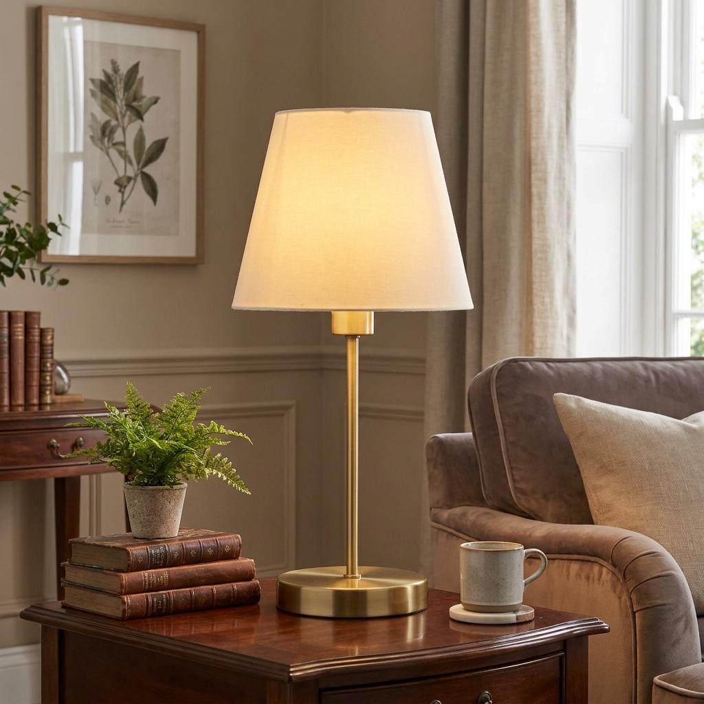 A brass table lamp with a cream tapered shade glows on a dark wood side table in a cozy, neutral-toned living room.