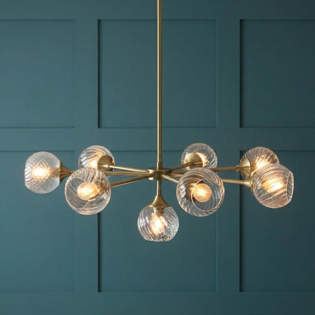 Allegra 8-light brass pendant with ribbed glass globes against a teal paneled wall.