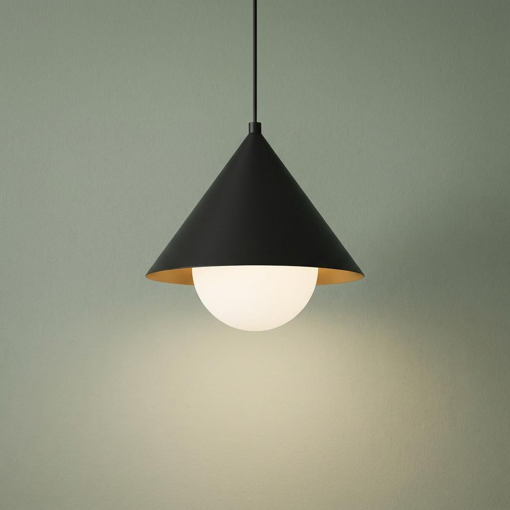 Modern black cone-shaped pendant light with an opal glass globe glowing against a sage green wall.