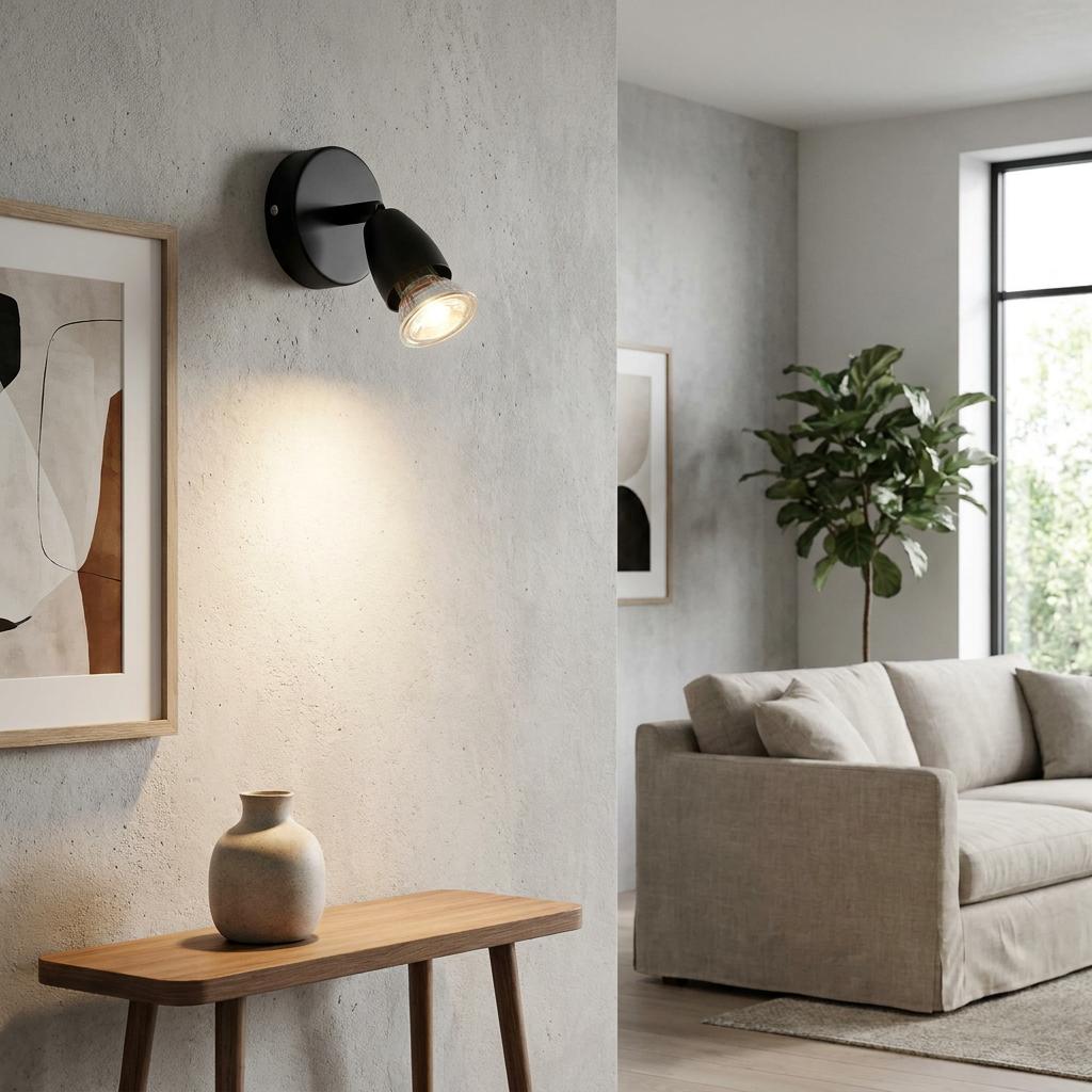 Black adjustable wall spotlight illuminates a textured wall above a wooden console in a minimalist living room.
