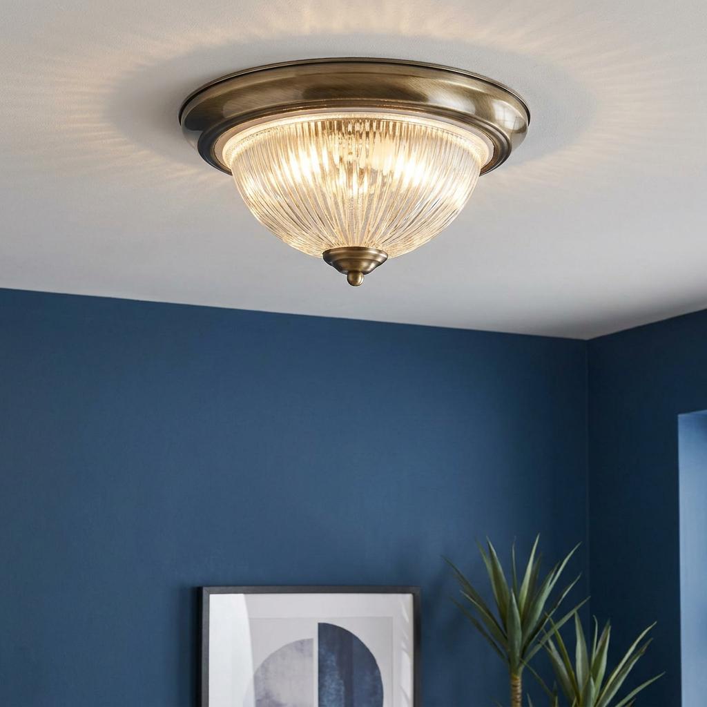 Antique brass flush-mount ceiling light with a ribbed glass dome glowing against a dark blue wall.