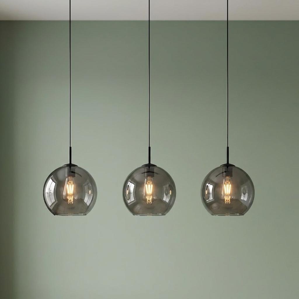 Three smoked glass globe pendant lights with warm bulbs hanging against a green wall.