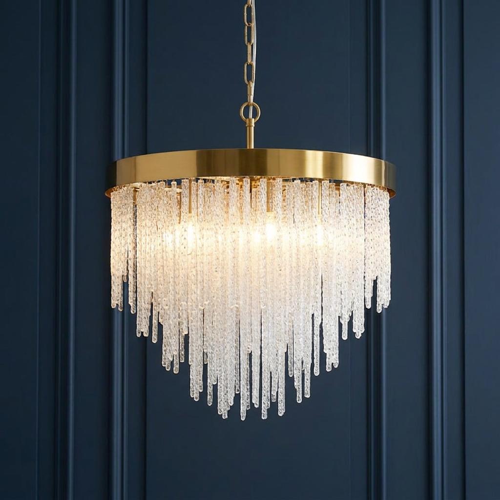 A brass pendant chandelier with tiered textured glass rods hanging in front of a dark blue paneled wall.