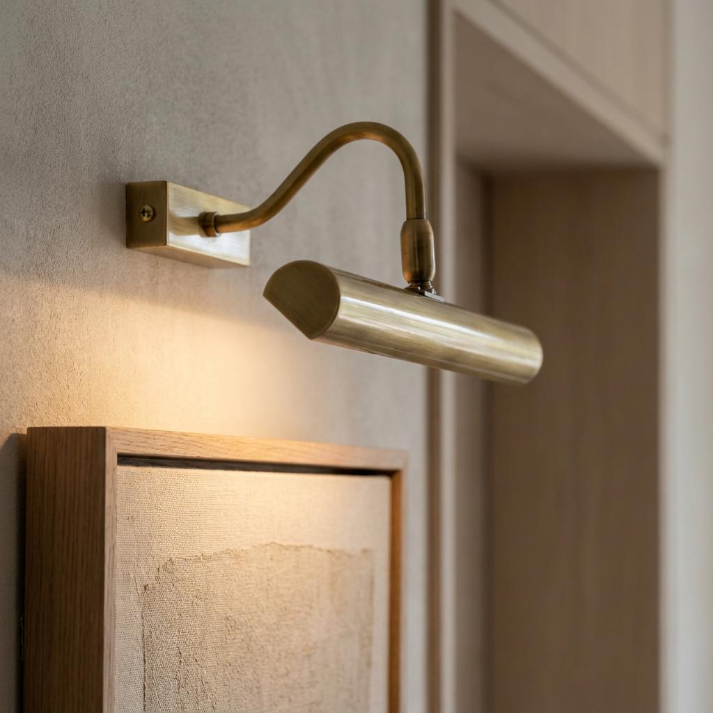 Antique brass picture light with a curved arm illuminating a canvas painting on a textured wall.