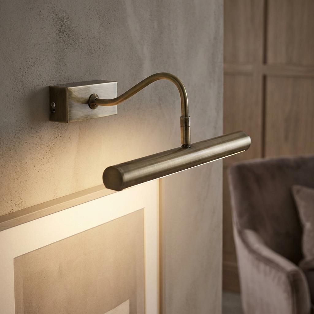 Antique brass picture light with a curved arm illuminating a framed picture on a neutral-toned wall.