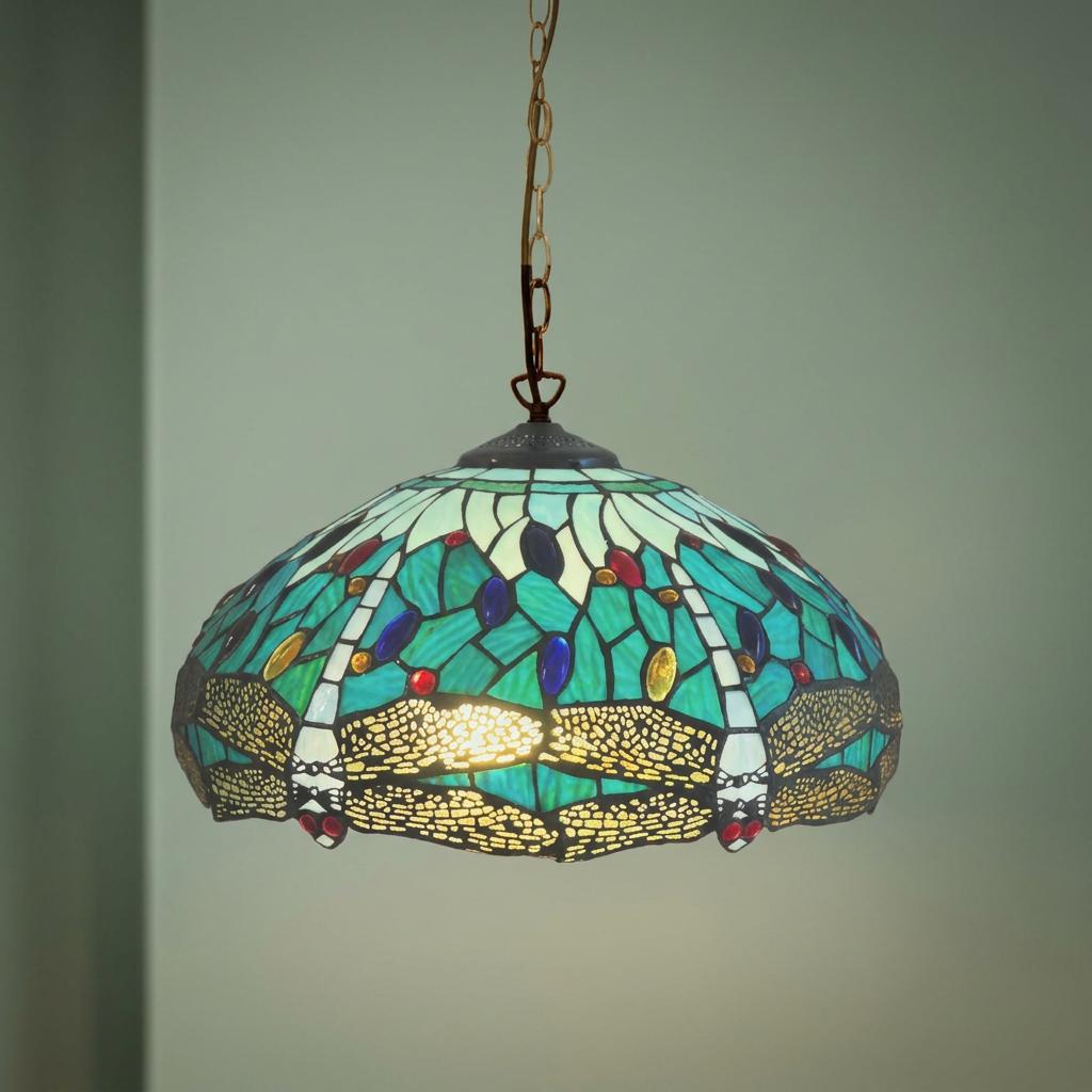 Aqua dragonfly Tiffany-style stained glass pendant light hanging from a chain against a plain green wall.