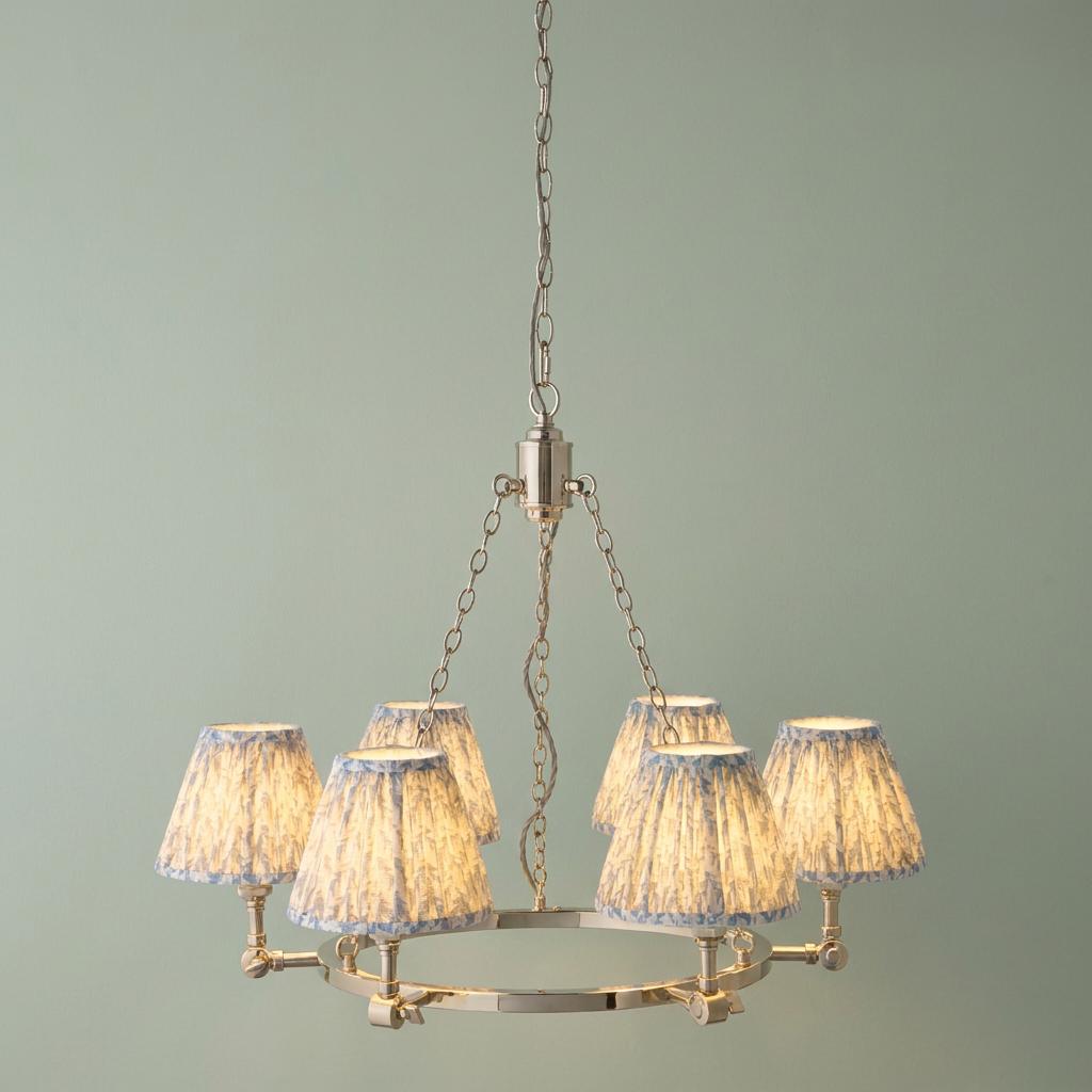 Bright nickel circular pendant light with six pleated blue fabric shades suspended against a soft green wall.